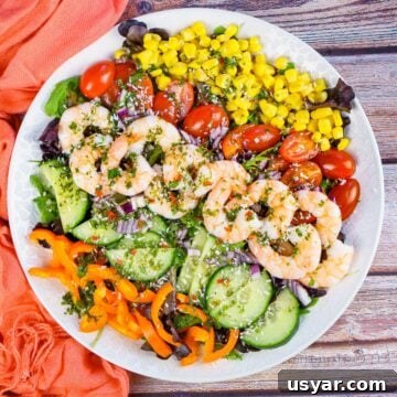 King Prawn Salad served on a white plate consisting of rocket leaves,sweet corn, chopped cherry tomatoes, cucumber, orange pepper, chilli salad dressing and sprinkled desiccated coconut all over the top