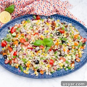 Italian Style Rice Salad on a large blue platter plate with lemon and basil on the side