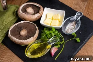 Two Portobello mushrooms, olive oil, cubes of butter, a garlic clove, salt, pepper and fresh parsley on a slate board