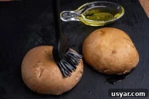 Spreading olive oil over two mushrooms using a pastry brush