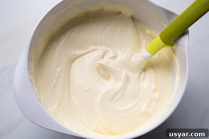 Creamy Banana Pudding Recipe with Sour Cream 6 whipped topping pudding mixture in a white mixing bowl with a green spatula.