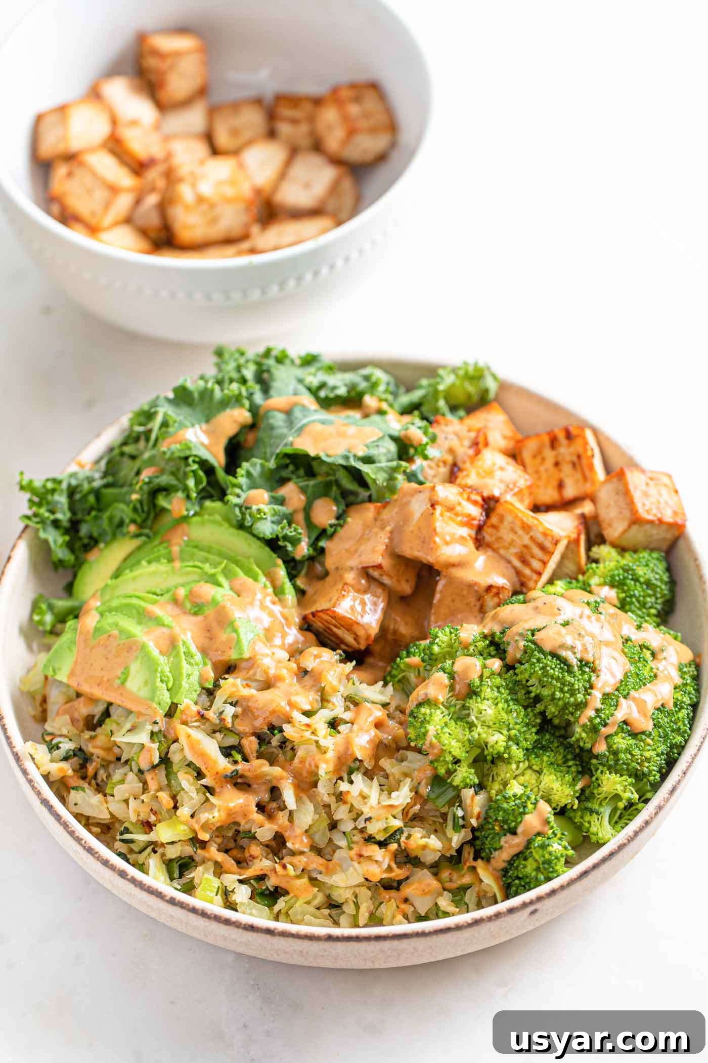 Bowl with cabbage, avocado, tofu, onion, kale and broccoli, topped with sauce.