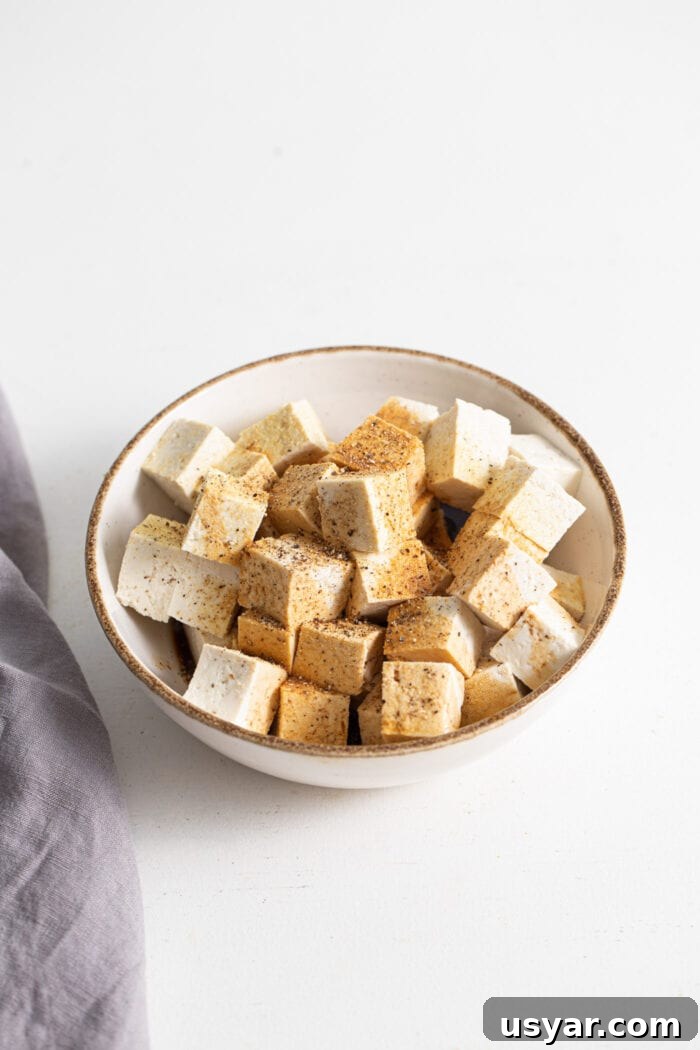 Cubed tofu in a bowl topped with garlic powder and black pepper.