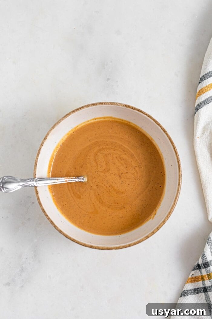 Bowl of creamy peanut sauce with a spoon in it.