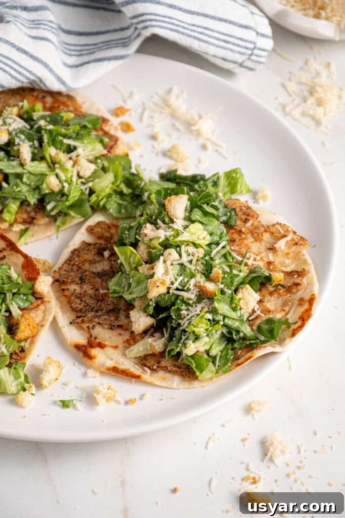 A plate with a smash chicken taco topped with chopped caesar salad with parmesan and crushed croutons.