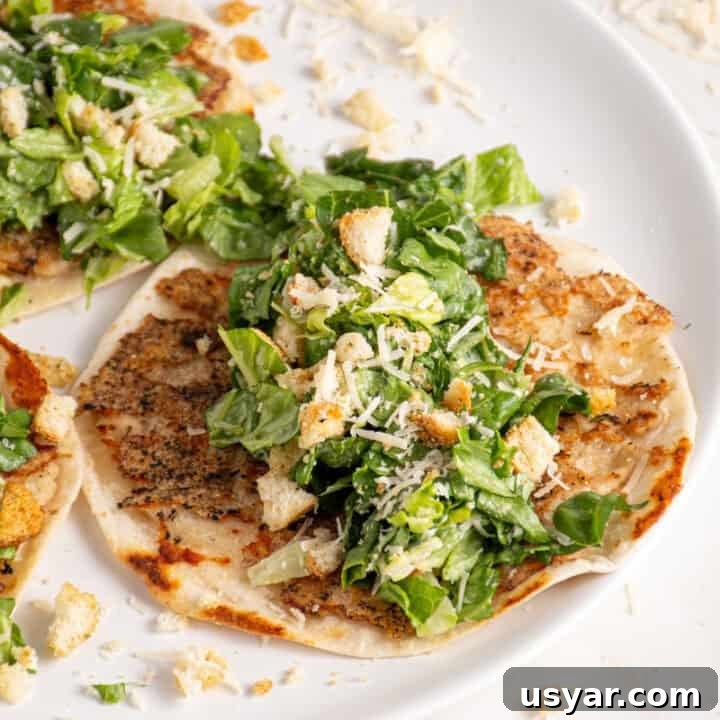 A plate with a smash chicken taco topped with chopped caesar salad with parmesan and crushed croutons.