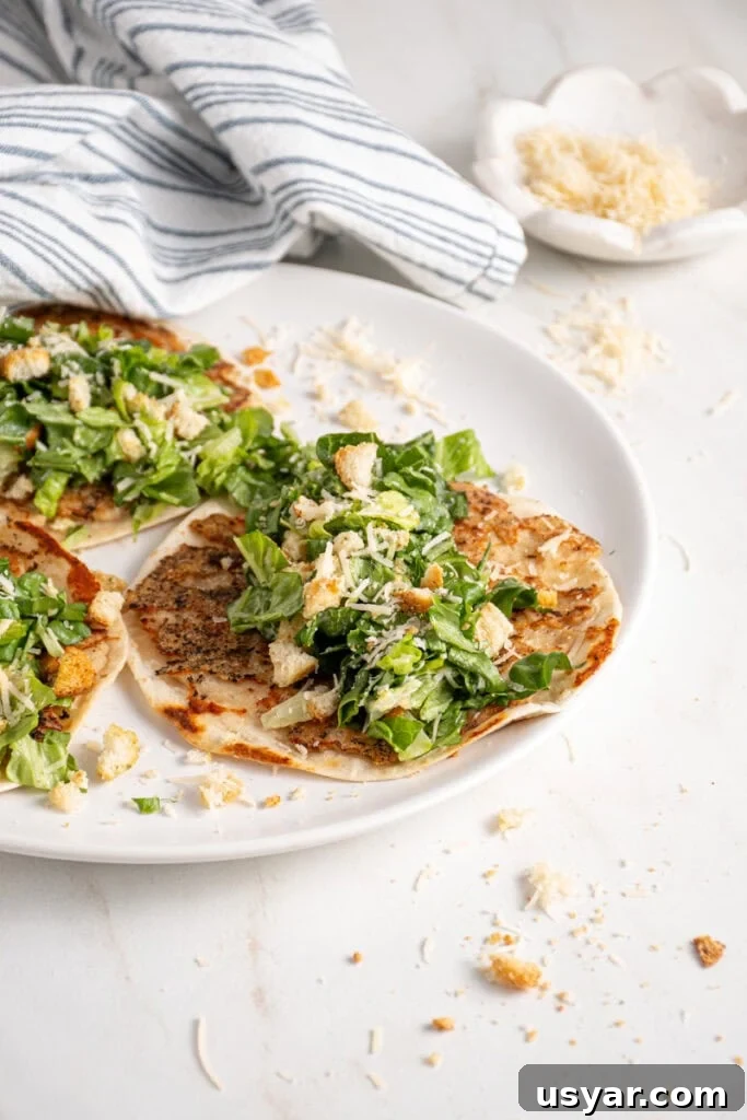 A plate with a smash chicken taco topped with chopped caesar salad with parmesan and crushed croutons.