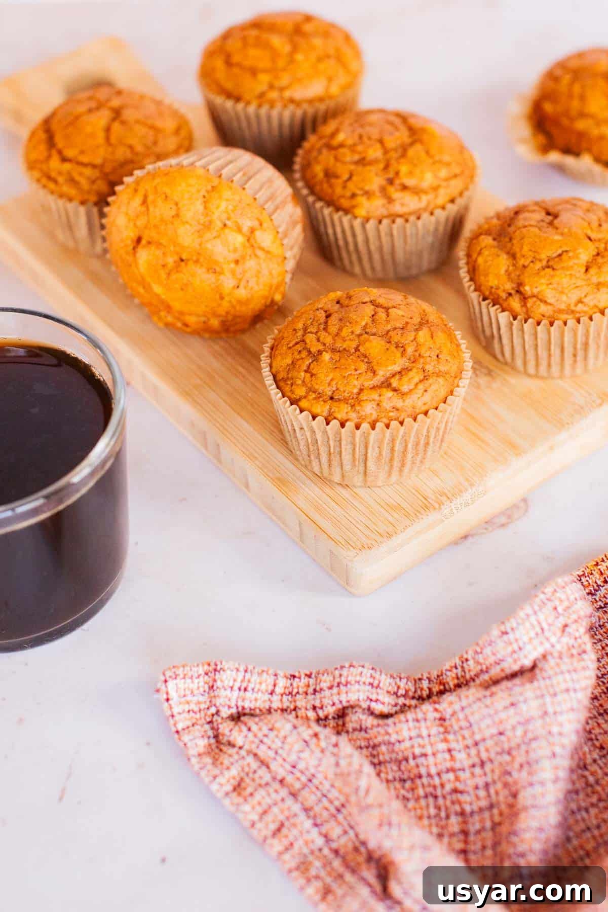 Moist Pumpkin Spice Muffins Recipe 5 Pumpkin muffins on a wooden serving dish next to a clear, glass mug filled with coffee.