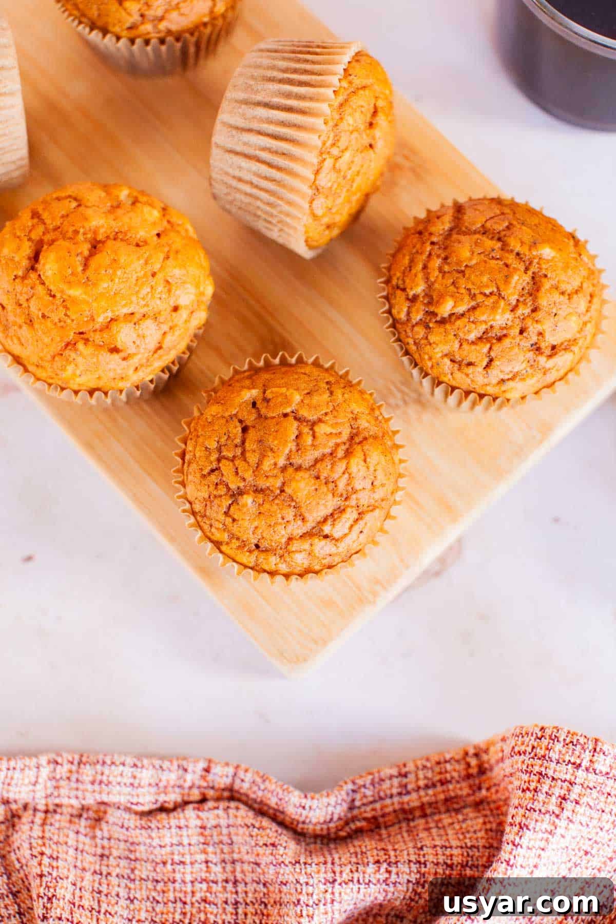 Moist Pumpkin Spice Muffins Recipe 6 Pumpkin muffins on a wooden serving dish arranged on a marble countertop.