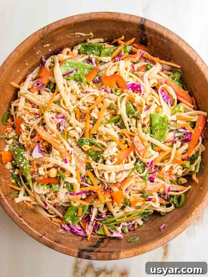 Wooden bowl with rice noodles and crunchy vegetables tossed with tahini dressing.