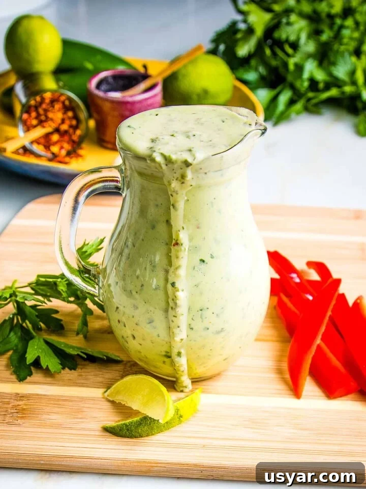 Pitcher of green tahini sauce dripping over the edge onto a board with cut up veggies.