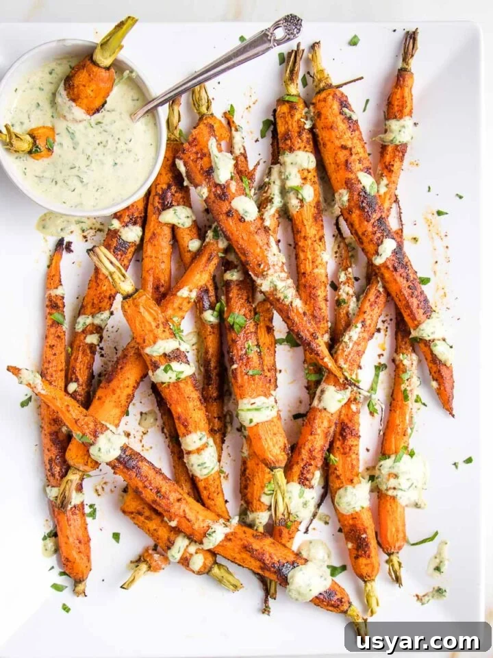 White platter with whole roasted carrots coated with spices and served with green tahini sauce.