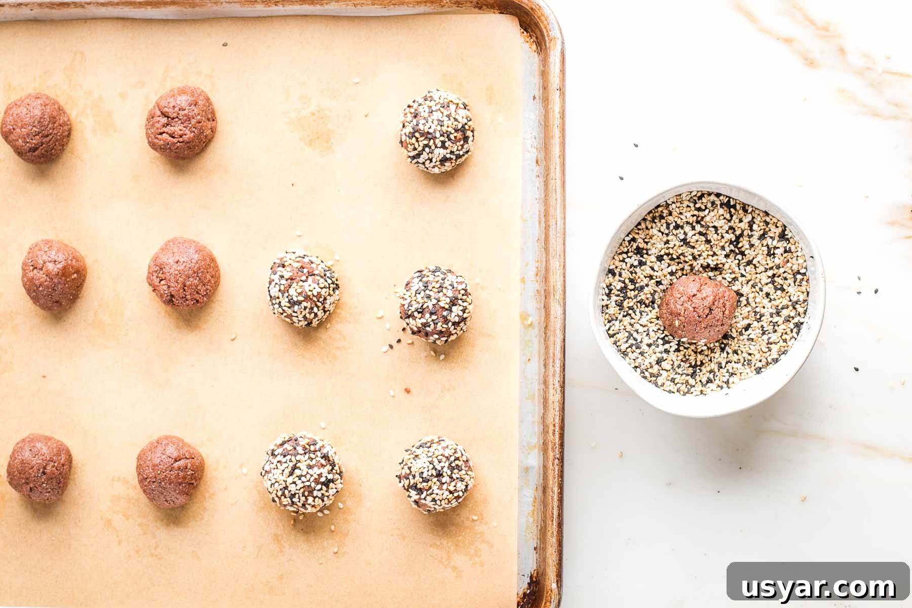 Crispy Sesame Seed Cookies Recipe 9 Baking tray with dark brown cookie dough balls, some already rolled into multi-colored sesame seeds.