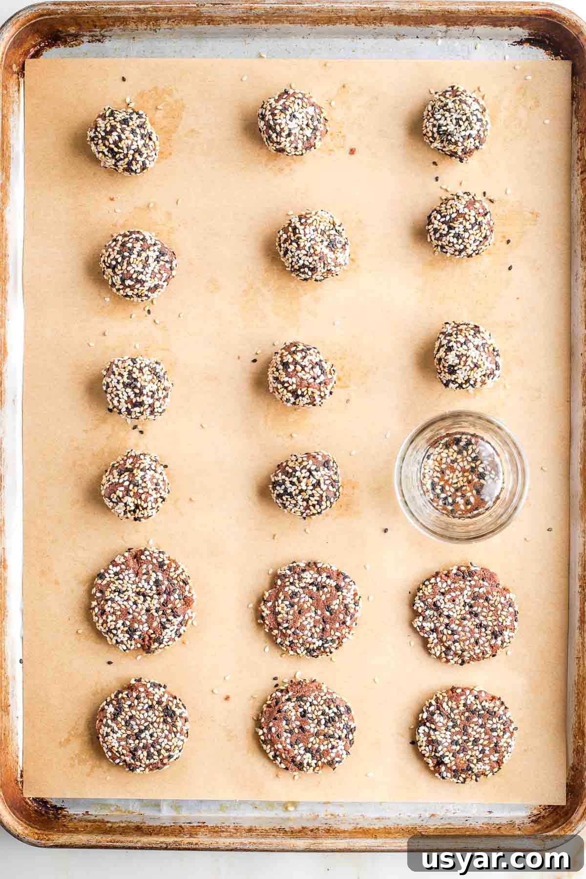 Crispy Sesame Seed Cookies Recipe 10 Cookie sheet filled with sesame seed coated cookies, being flattened by a glass.