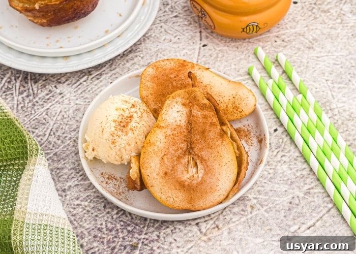 Crispy Honey-Glazed Pears in the Air Fryer 6 Cooked golden pear, served with vanilla ice cream, and sprinkled with cinnamon, served on a white plate.