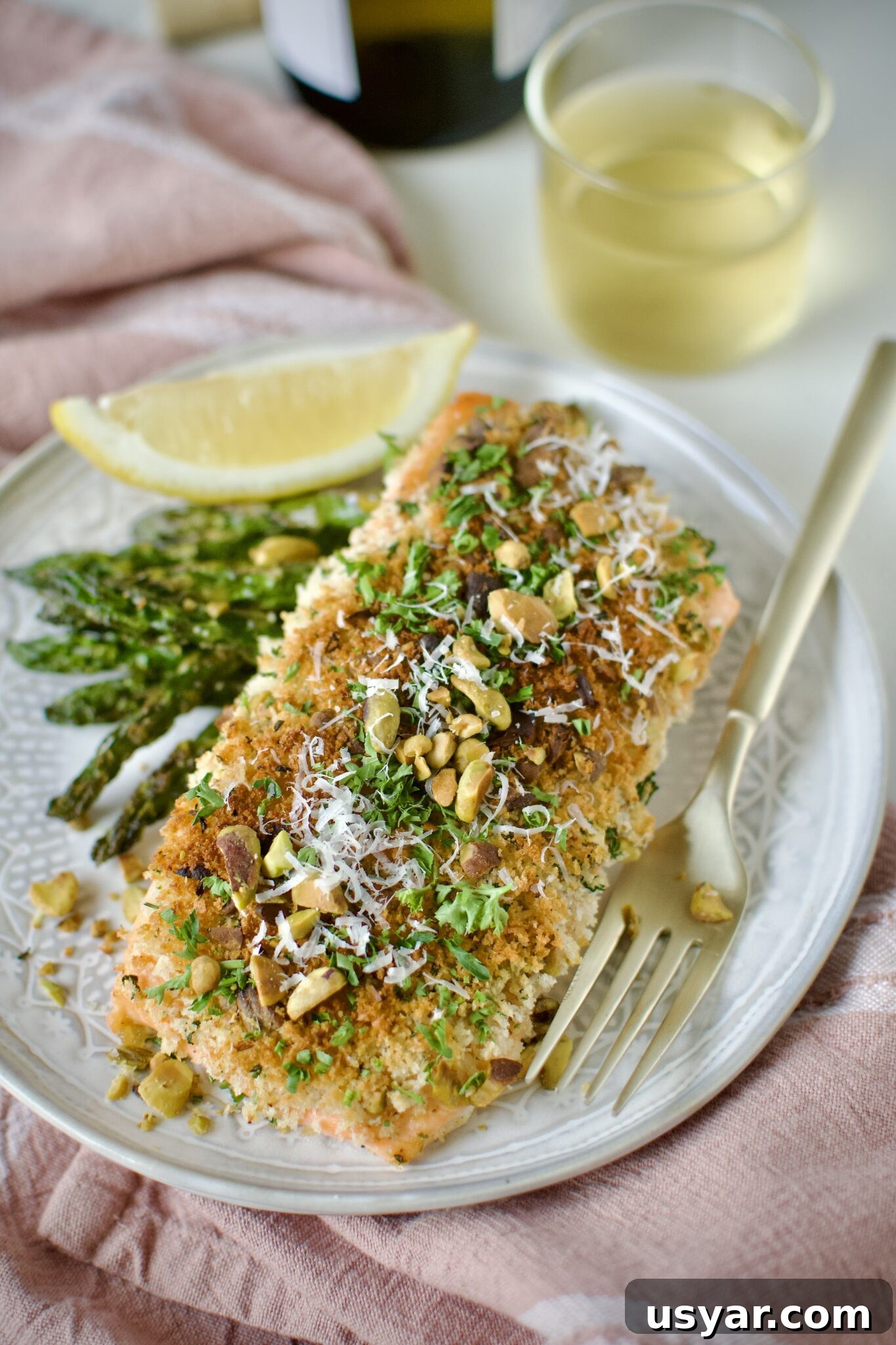 Pistachio Crusted Salmon on a plate with some grilled asparagus and a lemon wedge. Ready to eat.