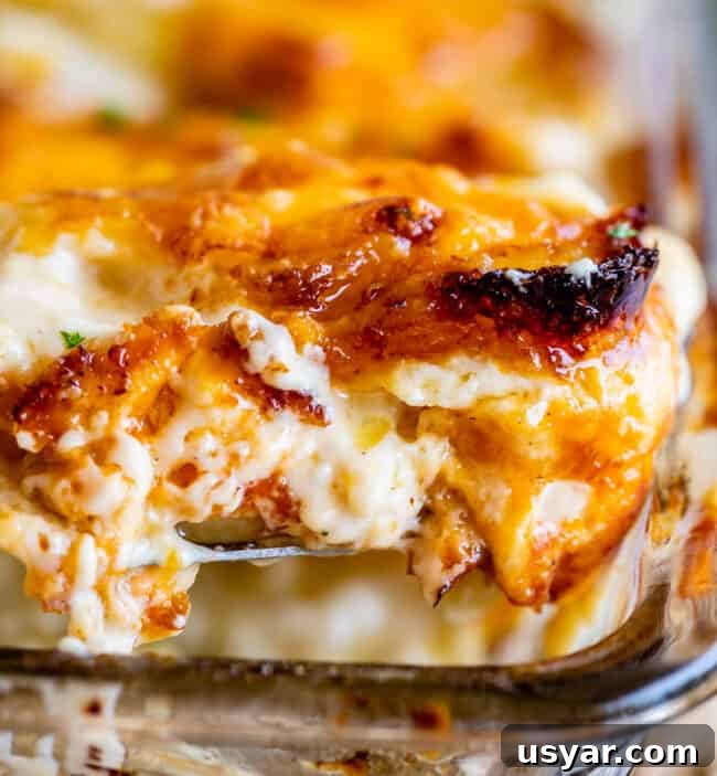 cheese scalloped potatoes with crispy edges being lifted from a clear casserole dish