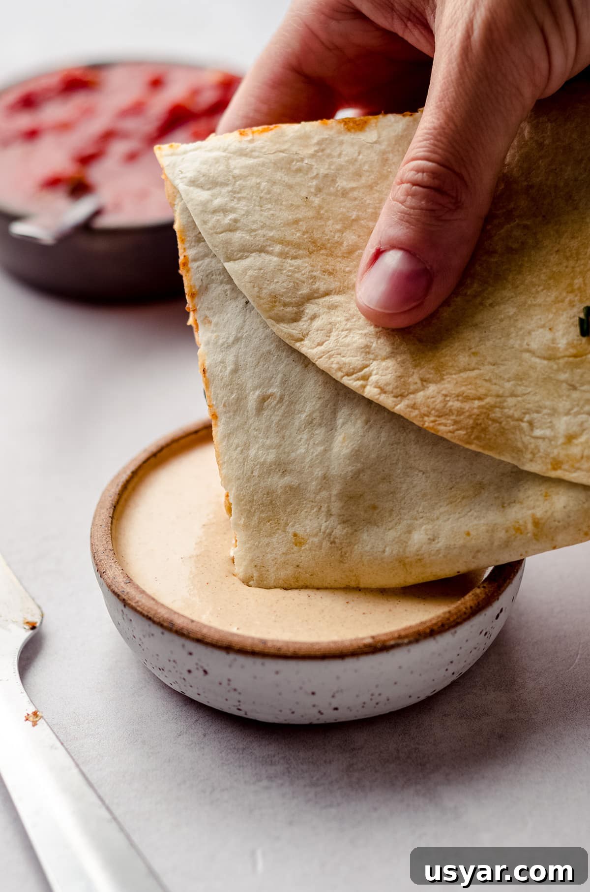 dipping sheet pan quesadillas into quesadilla sauce
