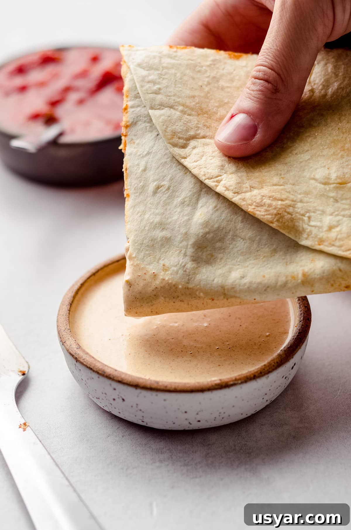 hand dipping homemade quesadillas into quesadilla sauce