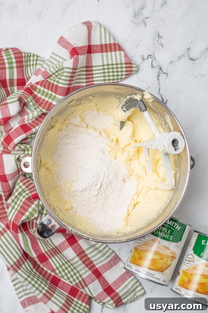 Cinnamon-Apple Pie Bars with Vanilla Glaze 6 Flour is added to butter mixture in mixing bowl from stand mixture.