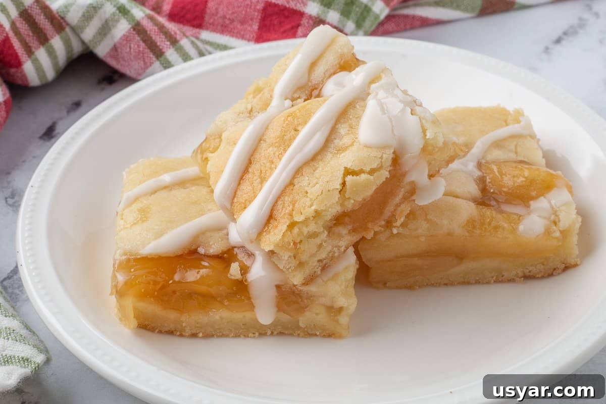 Cinnamon-Apple Pie Bars with Vanilla Glaze 8 Three apple pie bars on white plate with vanilla glaze.