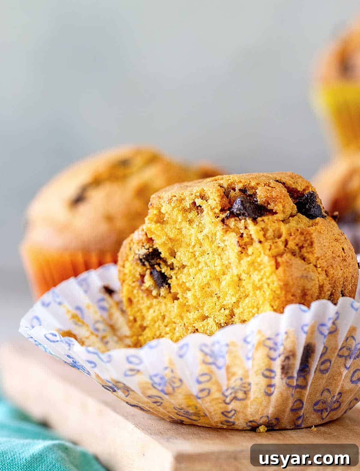 Half pumpkin muffin in opened paper liner on a wooden board.