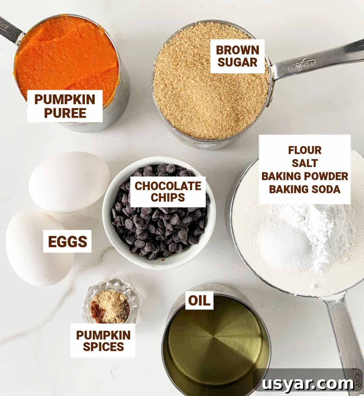 White surface with bowls containing ingredients for pumpkin chocolate chip muffins including oil, sugar, flour, eggs, spices.
