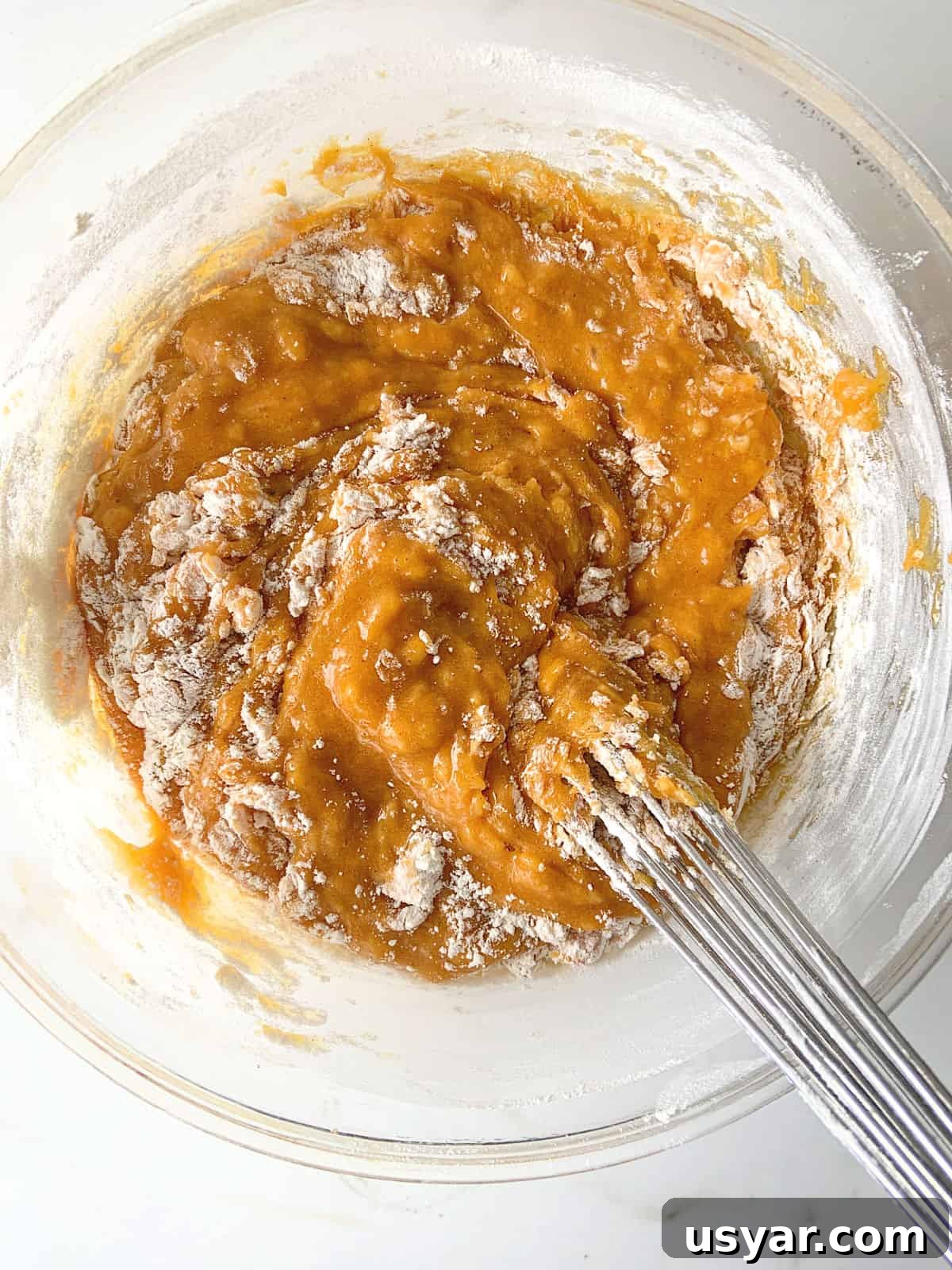 Flour being incorporated in pumpkin batter, metal whisk and glass bowl