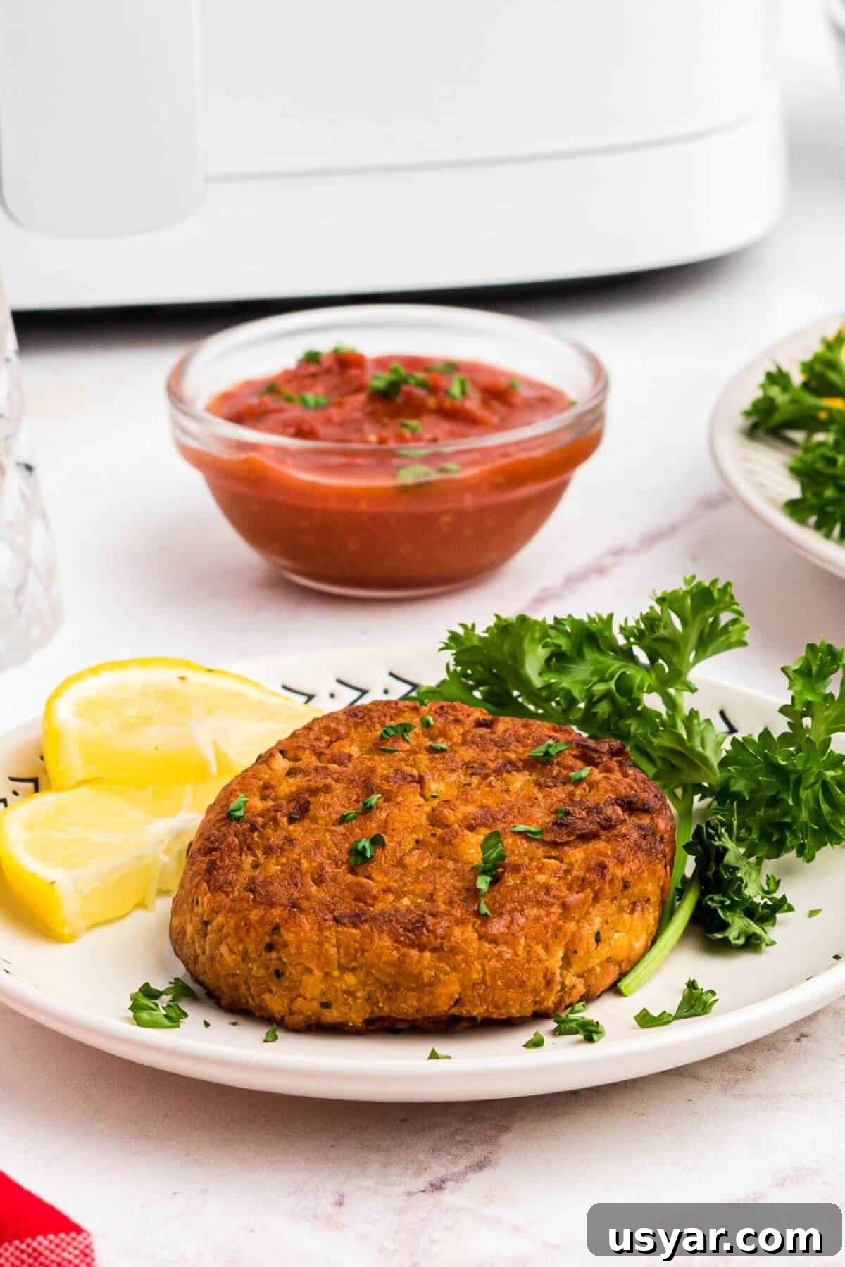 golden brown fried crab cakes on a small plate with parsley and lemon in front of an air fryer. 