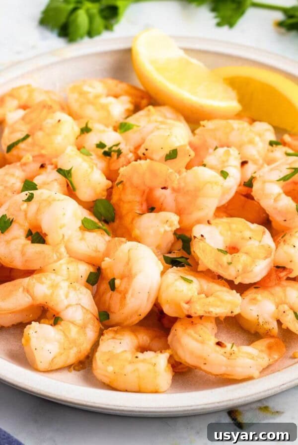 Orange shrimp stacked on a white plate with lemon wedges.