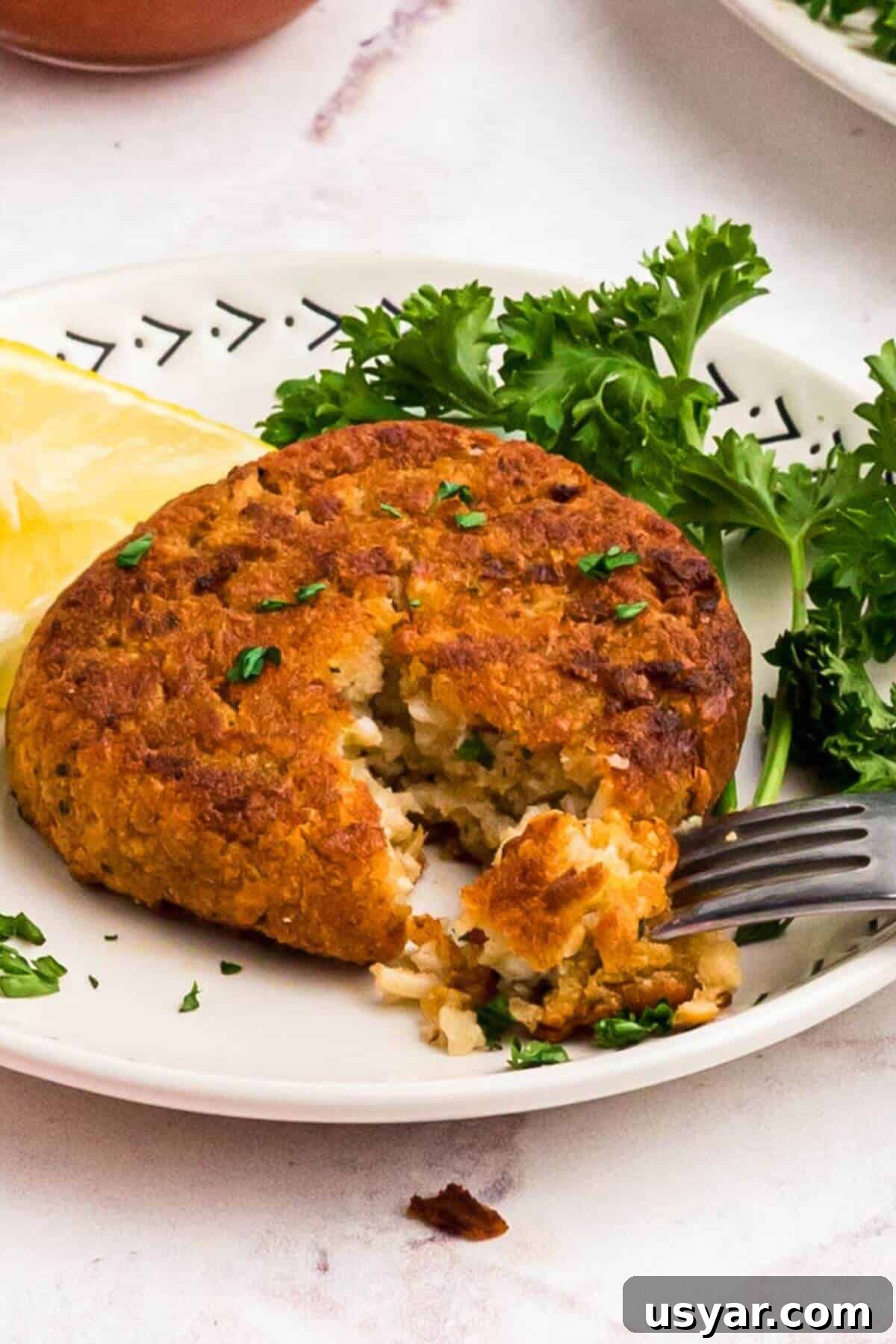 Golden crispy crab cake on a small plate with a fork taking a small piece. 