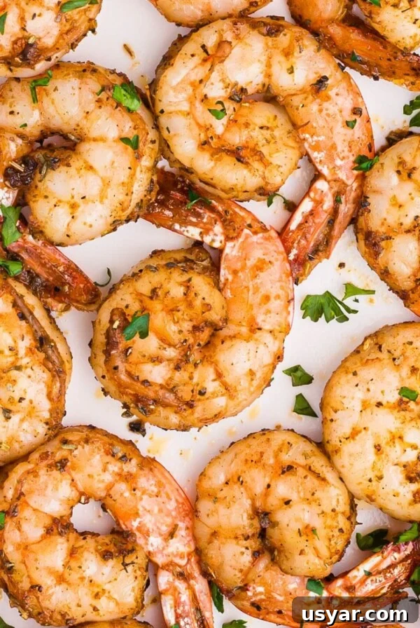 Juicy seasoned shrimp on a white plate garnished with parsley flakes