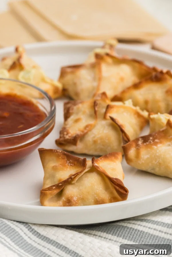 Air Fryer Crab Rangoon on a white plate with dipping sauce on the side.