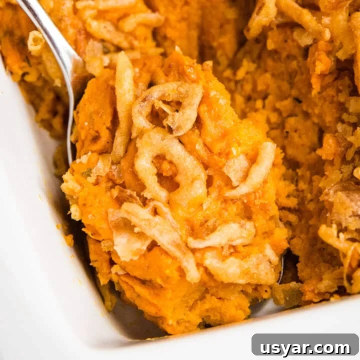 A close up of a serving spoon in a pan of savory sweet potato casserole.