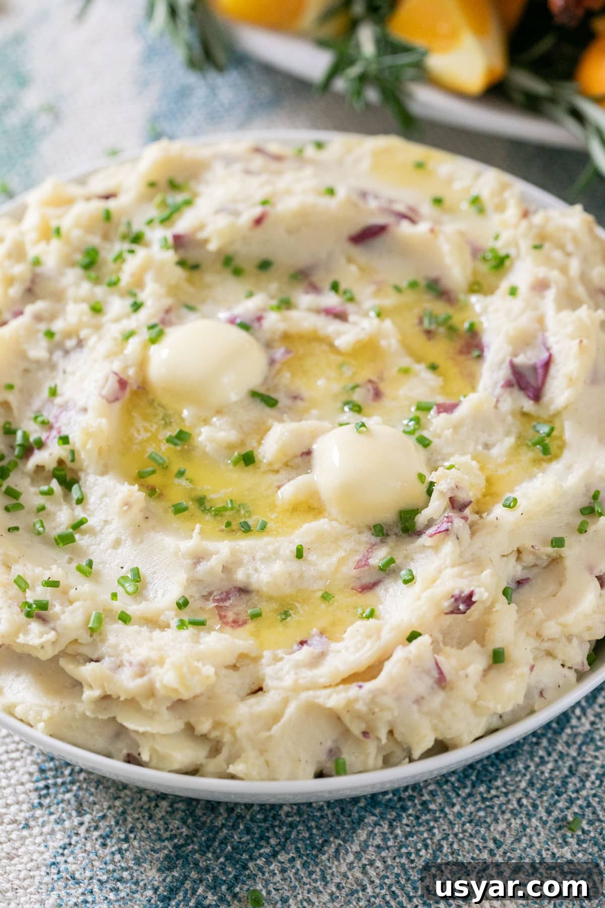 Creamy Gouda Mashed Potatoes 3 A close up image of mashed potatoes with butter and chives in a white bowl.