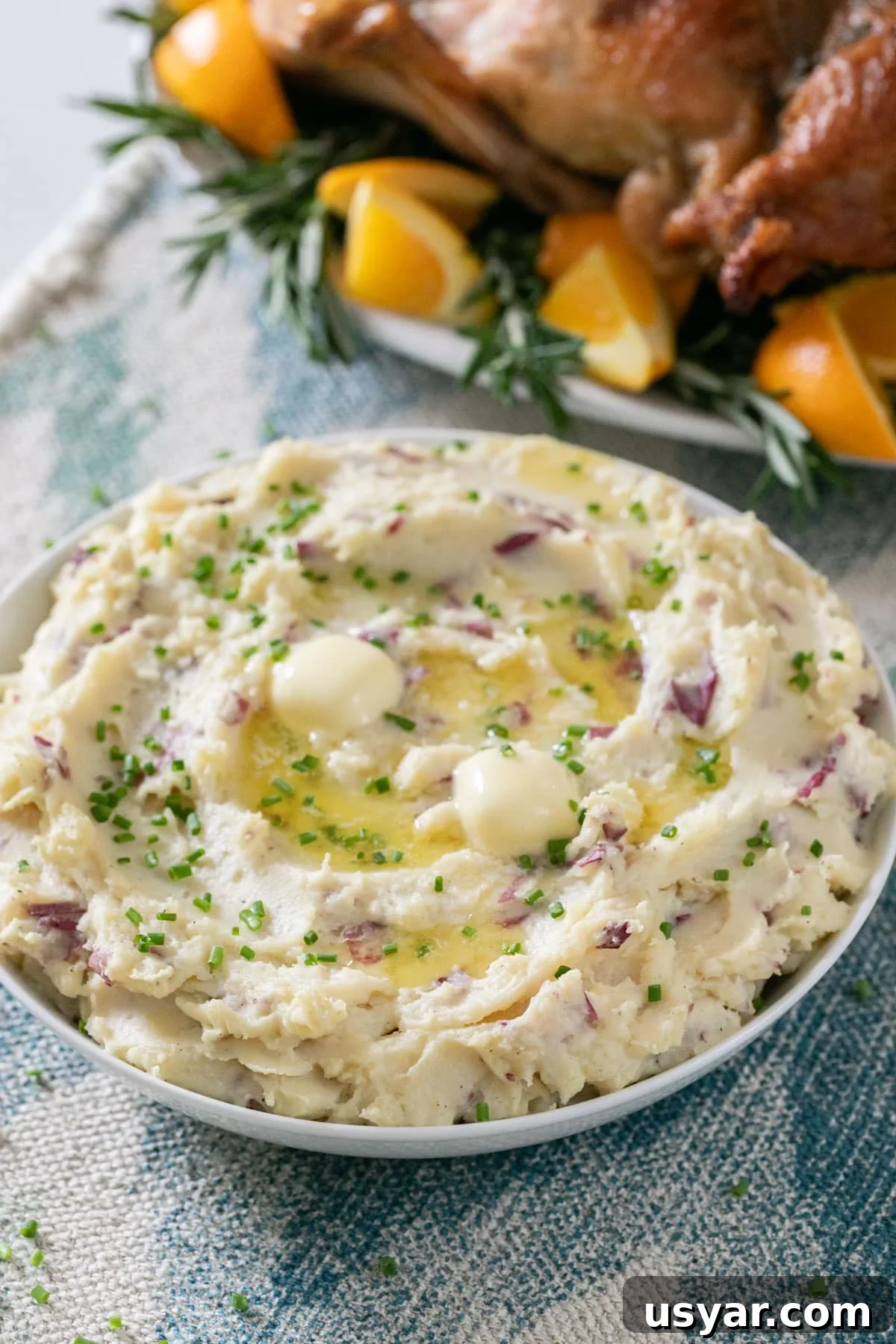 Creamy Gouda Mashed Potatoes 8 A bowl of mashed potatoes on a Thanksgiving table with the turkey platter behind it.