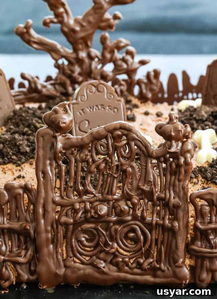 A chocolate Halloween Cake with gate, fence, tree and tombstones.