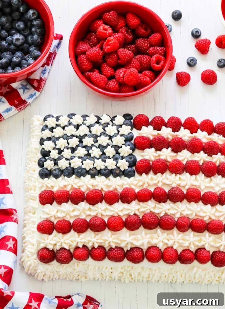An American flag cake decorated with blueberries, raspberries, and white frosting with a patriotic star towel.