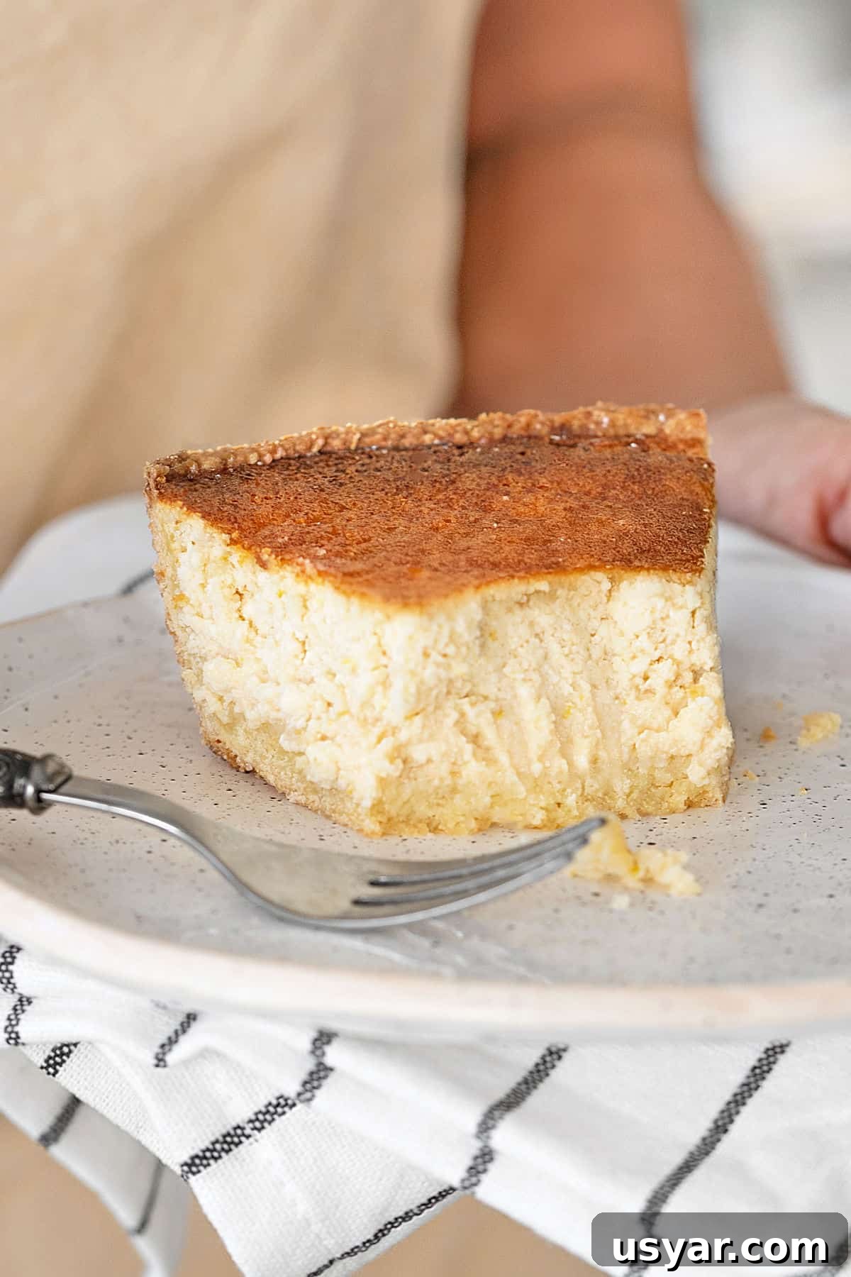 Amazing Lemon ricotta pie Forked slice of ricotta pie held on a white plate. Gray white striped cloth.