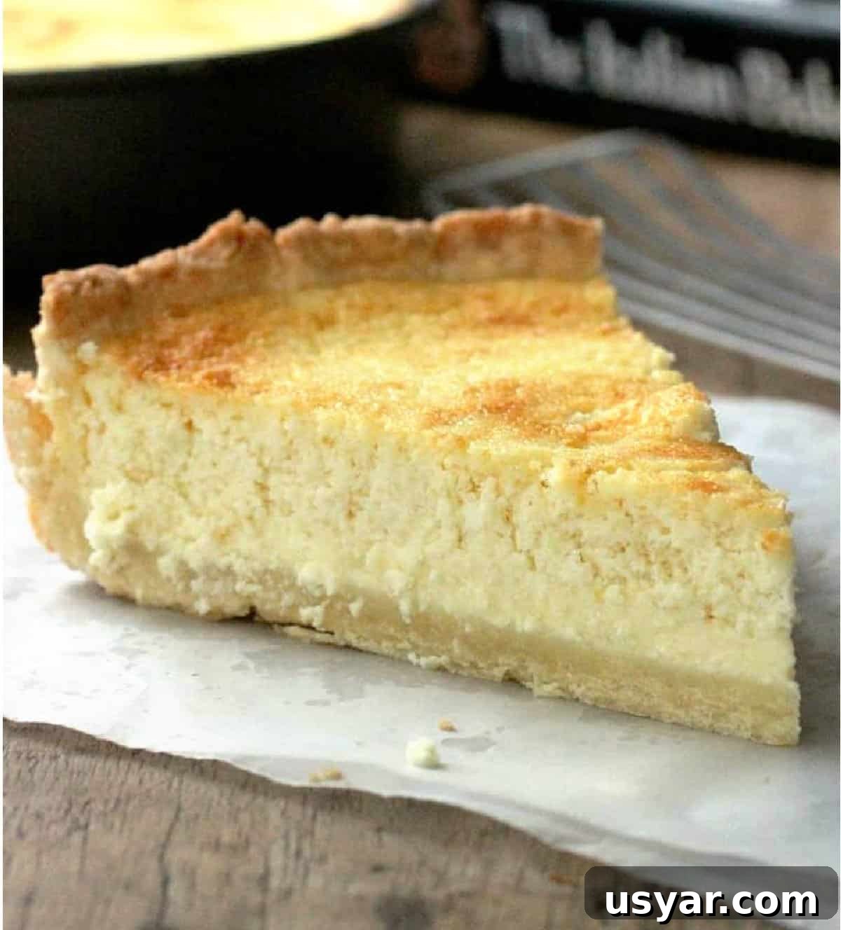 Lemon ricotta pie One slice of ricotta pie on parchment paper, pan and book in background