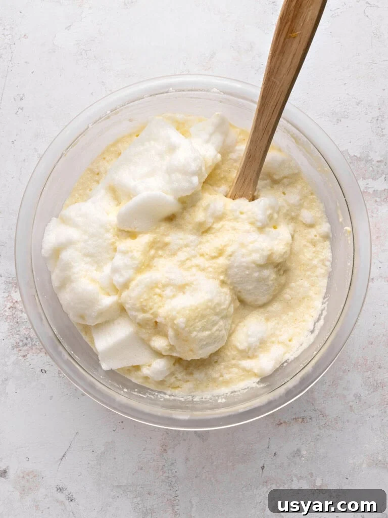 Classic Italian Ricotta Pie Recipe 7 Beaten egg whites with ricotta filling in a glass bowl. Wooden spatula. Light gray background.