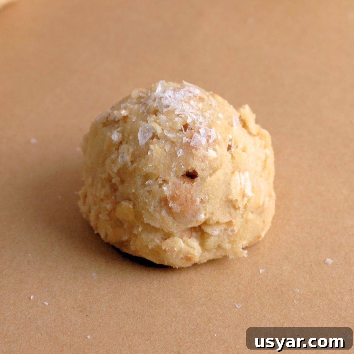 How to Make Chewy Salted Caramel Oatmeal Cookies 9 Dough ball for caramel oatmeal cookies topped with sea salt.