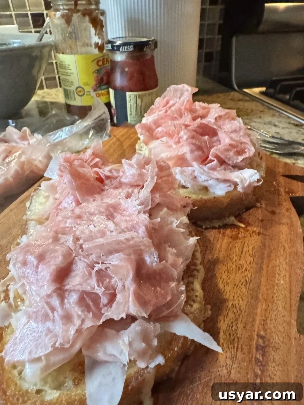 Open-Faced Italian Subs Recipe with Melty Mozzarella 3 Deli meats spit be tween two breads on a wooden cutting board.
