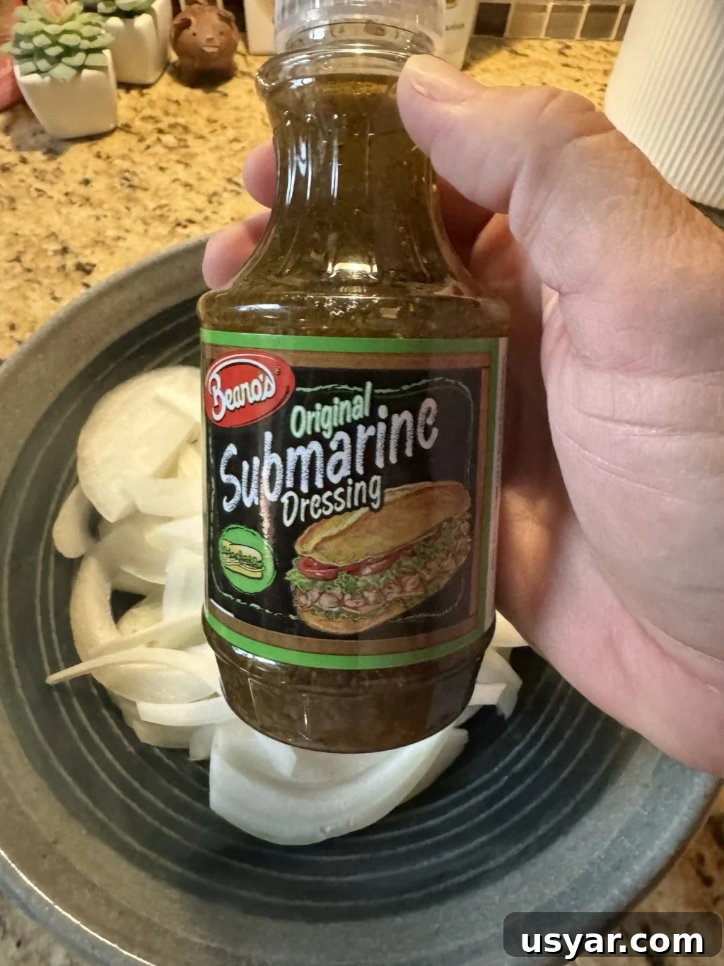Open-Faced Italian Subs Recipe with Melty Mozzarella 5 A bottle of Beano's Original Submarine Dressing held over a plate of onions.