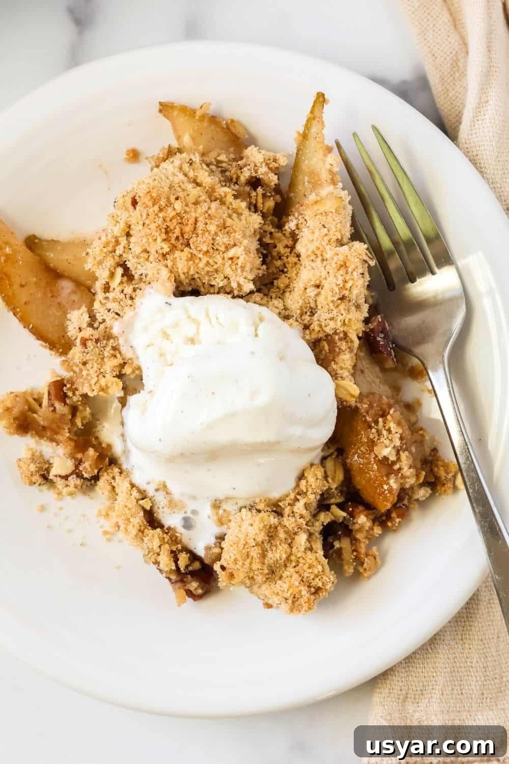 Warm Fresh Pear Crisp Recipe with Cinnamon Oat Topping 3 overhead view of cinnamon pear crumble served on a white plate, topped with ice cream. A fork is on the plate.