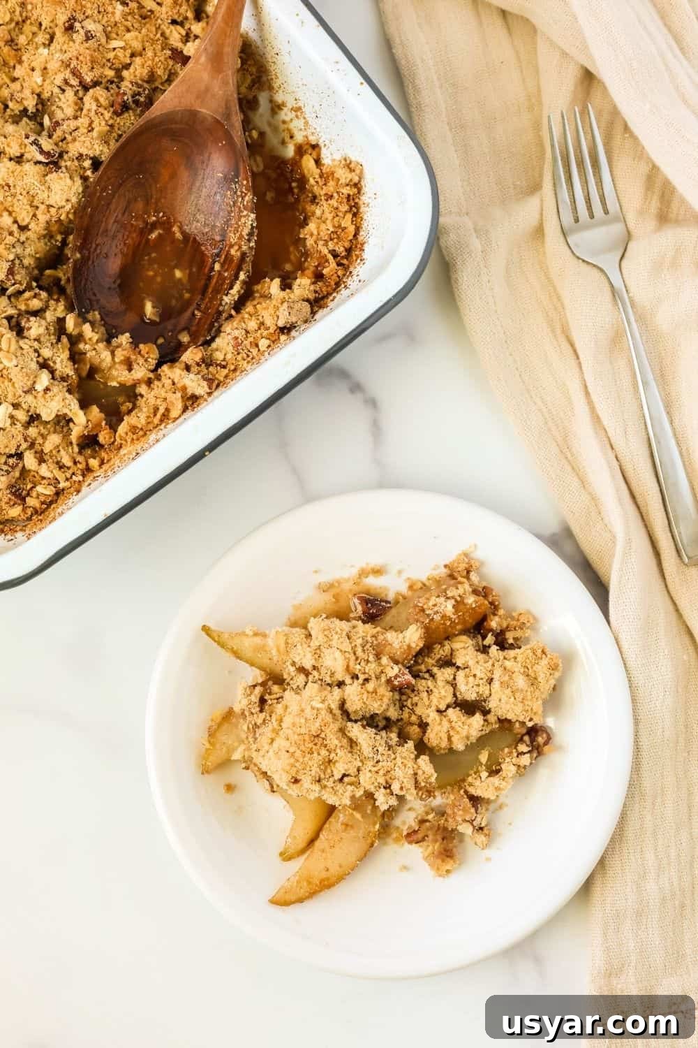 Warm Fresh Pear Crisp Recipe with Cinnamon Oat Topping 5 overhead view of a small dessert plate with a serving of pear cobbler with crumble topping. The pan of pear crisp is in the background.