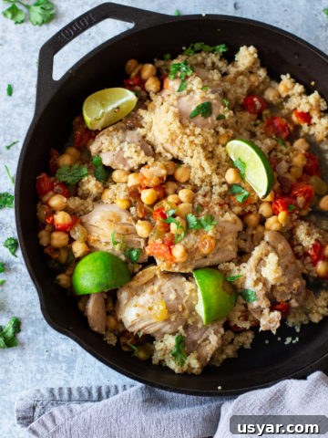 Cast iron skillet with chicken, chickpeas, tomatoes, limes, and parsley.