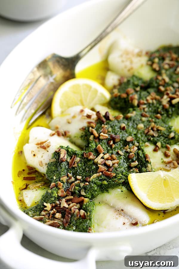 Oven-Baked Tilapia with Spinach Pecan Pesto Recipe 3 Close-up photo of Baked Tilapia with Spinach Pecan Pesto in white baking dish garnished with chopped pecans and lemon wedges.