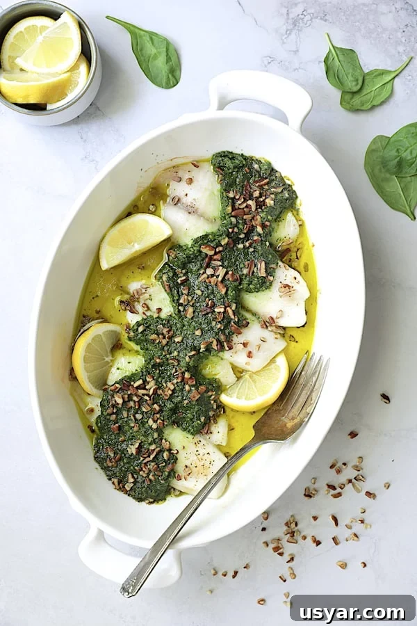 Oven-Baked Tilapia with Spinach Pecan Pesto Recipe 7 Photo of Baked Tilapia with Spinach Pecan Pesto on light gray background garnished with pecans and lemon wedges.