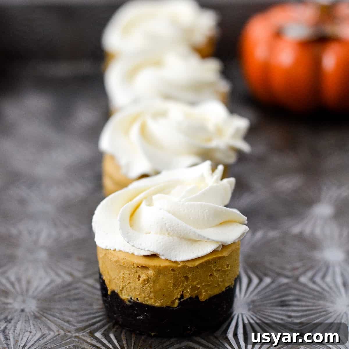 No-Bake Mini Vegan Pumpkin Pies are the perfect elegant fall dessert! They are gluten-free, dairy-free, refined sugar free, paleo, vegan and SUPER easy to make! #vegan #pumpkinpie #nobake #dessert #paleo #glutenfree #dairyfree Side view of 4 vegan pumpkin bites in a row. There is an orange pumpkin in the top right corner.